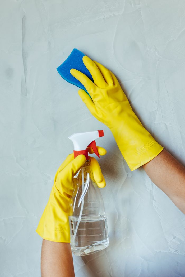 project-01-c Hands in yellow gloves cleaning wall with sponge and spray bottle.